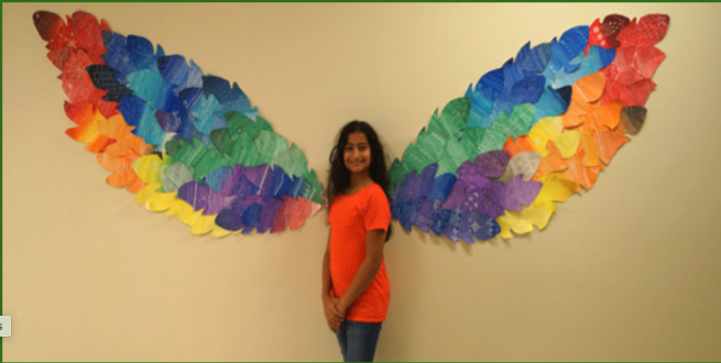 A girl stands between colour paper that has been hung on the wall behind her to look like wings.